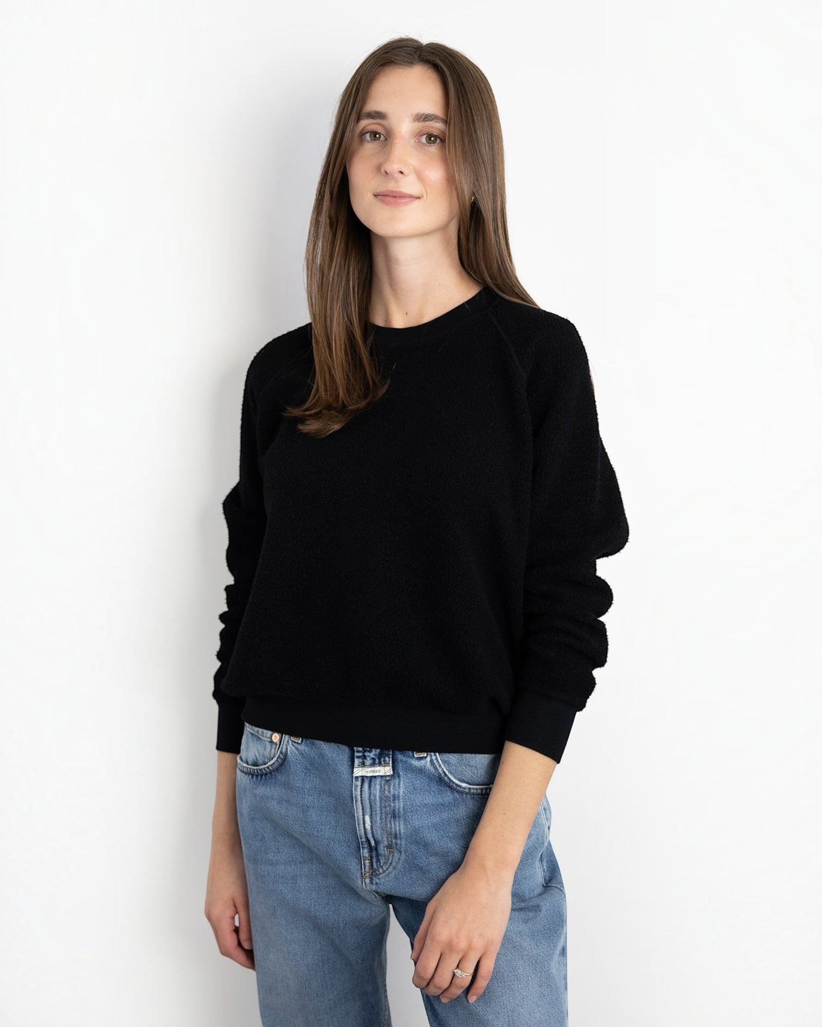 Model wearing a JONES + CO black Ziggy sweatshirt with a shrunken fit and cropped sleeves, paired with blue jeans.