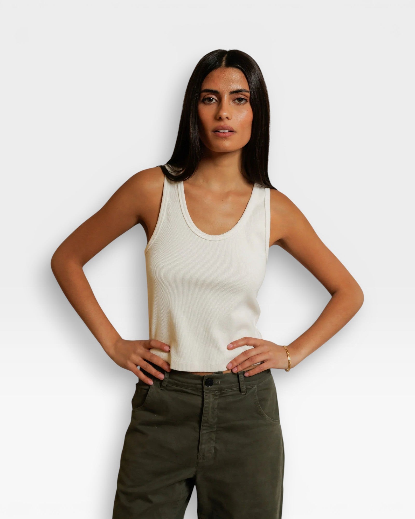 JONES + CO Blondie bright ivory ribbed tank top worn by a woman with hands on hips, styled with olive green pants.