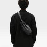 JONES + CO Bon-Bon M black calf leather crossbody bag with pleated ends and metal clasp worn on a model's back
