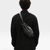 JONES + CO Bon-Bon M black calf leather crossbody bag with pleated ends and metal clasp worn on a model's back