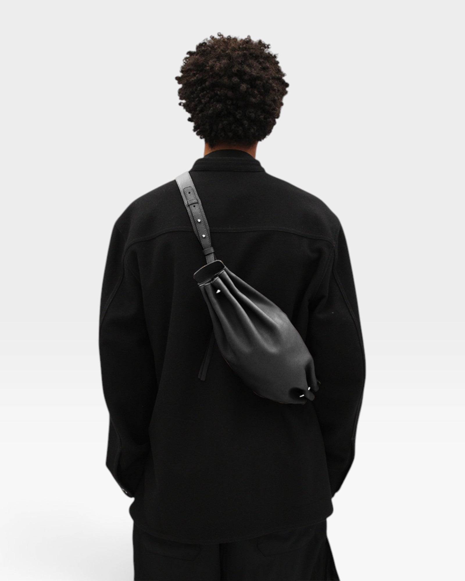 JONES + CO Bon-Bon M black calf leather crossbody bag with pleated ends and metal clasp worn on a model's back