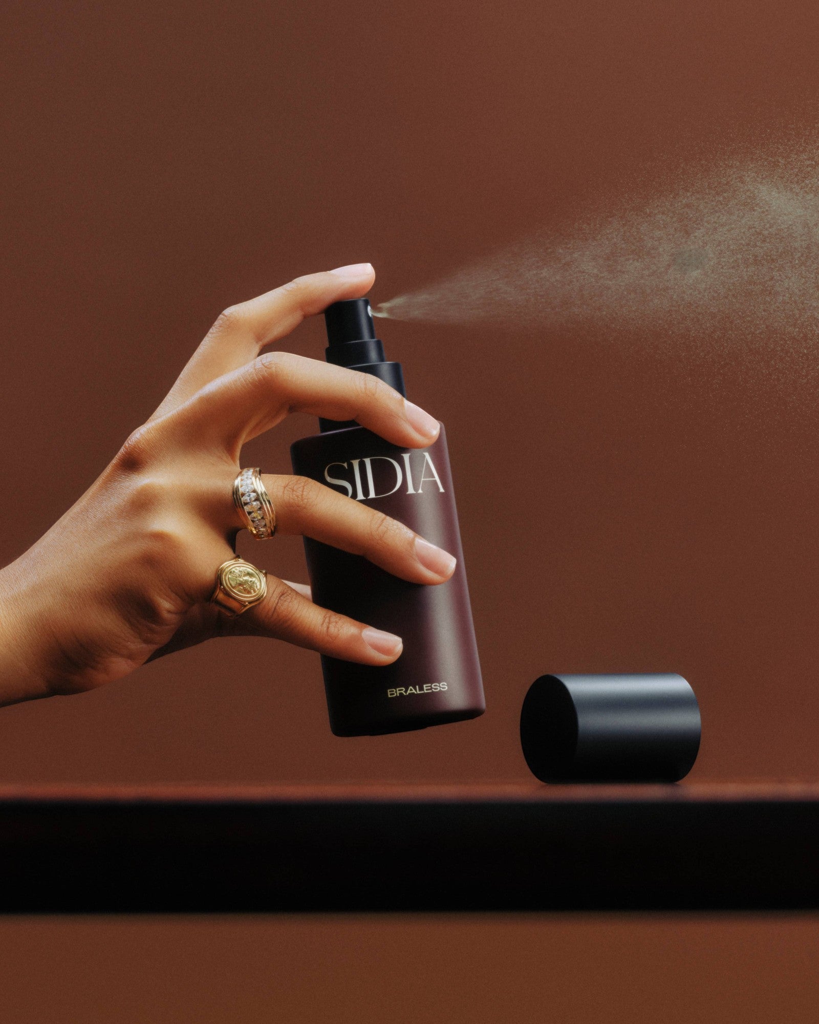 JONES + CO BRALESS body mist being sprayed by a hand with rings. The mist is a dark plum color.