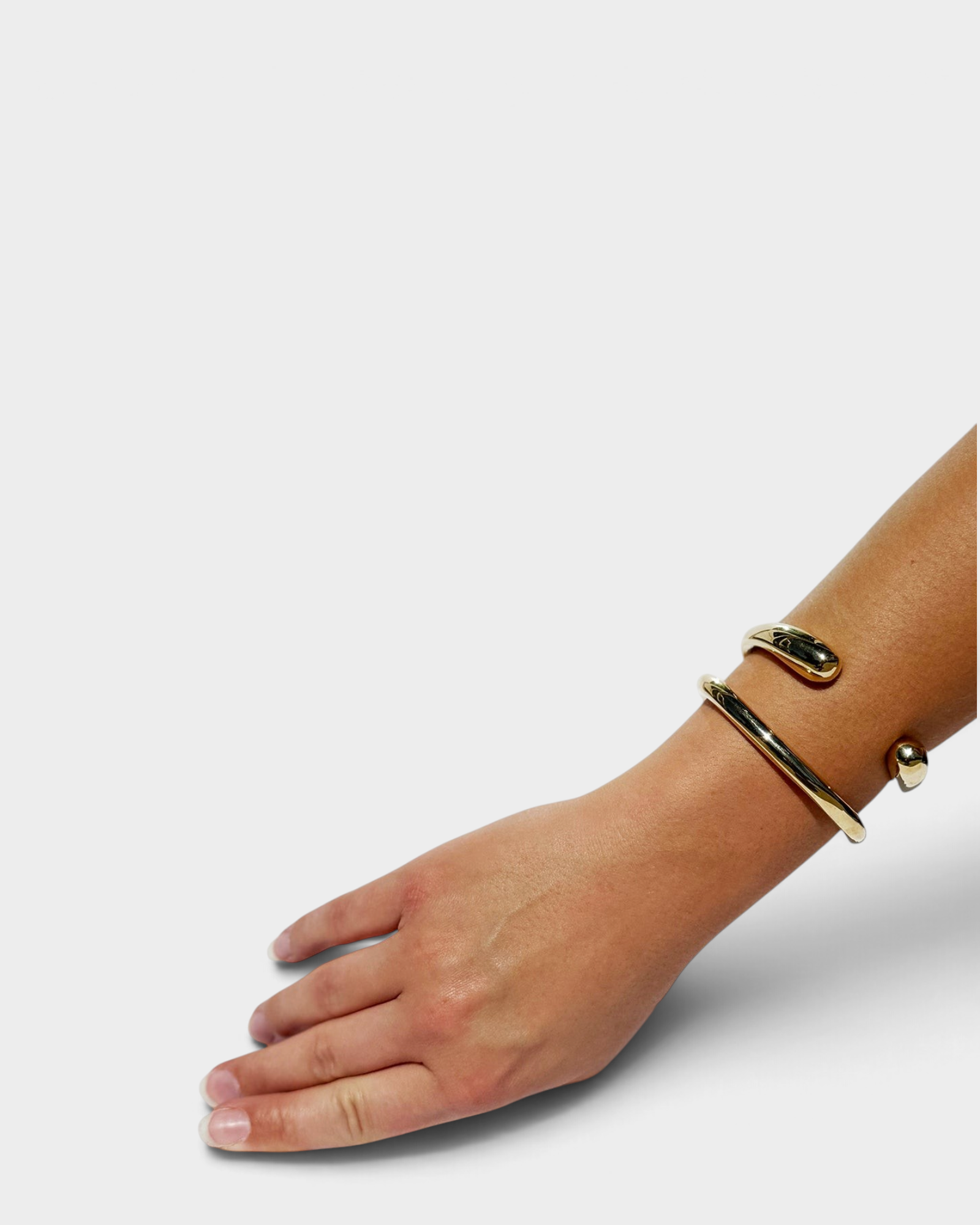 JONES + CO polished brass cuff bracelet worn on a woman's wrist, featuring a minimalist open-ended design.