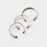 Three JONES + CO minimalist brass cuff bracelets with rounded ends arranged in a stackable set.