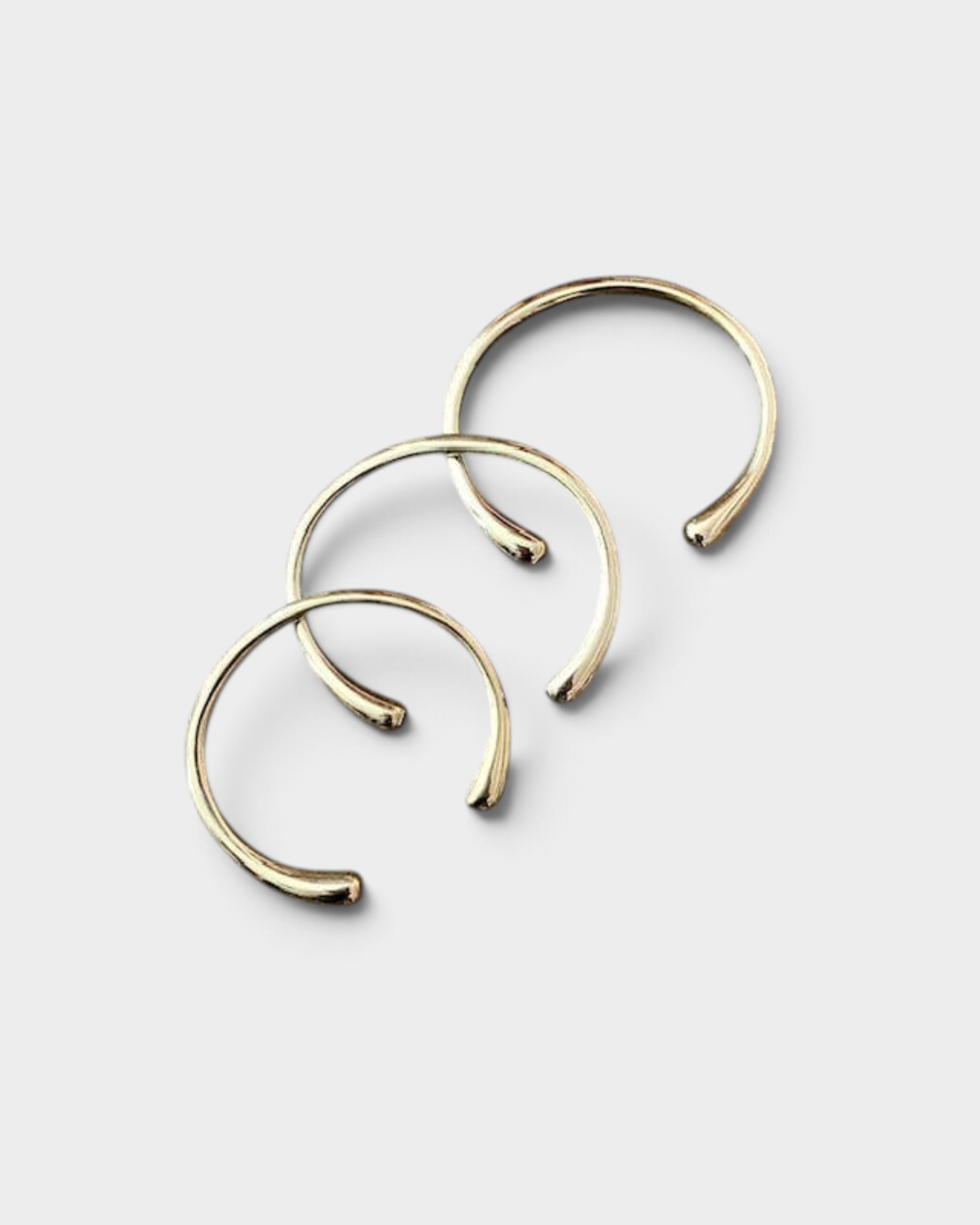 Three JONES + CO minimalist brass cuff bracelets with rounded ends arranged in a stackable set.