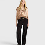 Model wearing a JONES + CO bronze sleeveless Hildra blouse with a V-neck, shawl collar, and fluid laminated fabric.