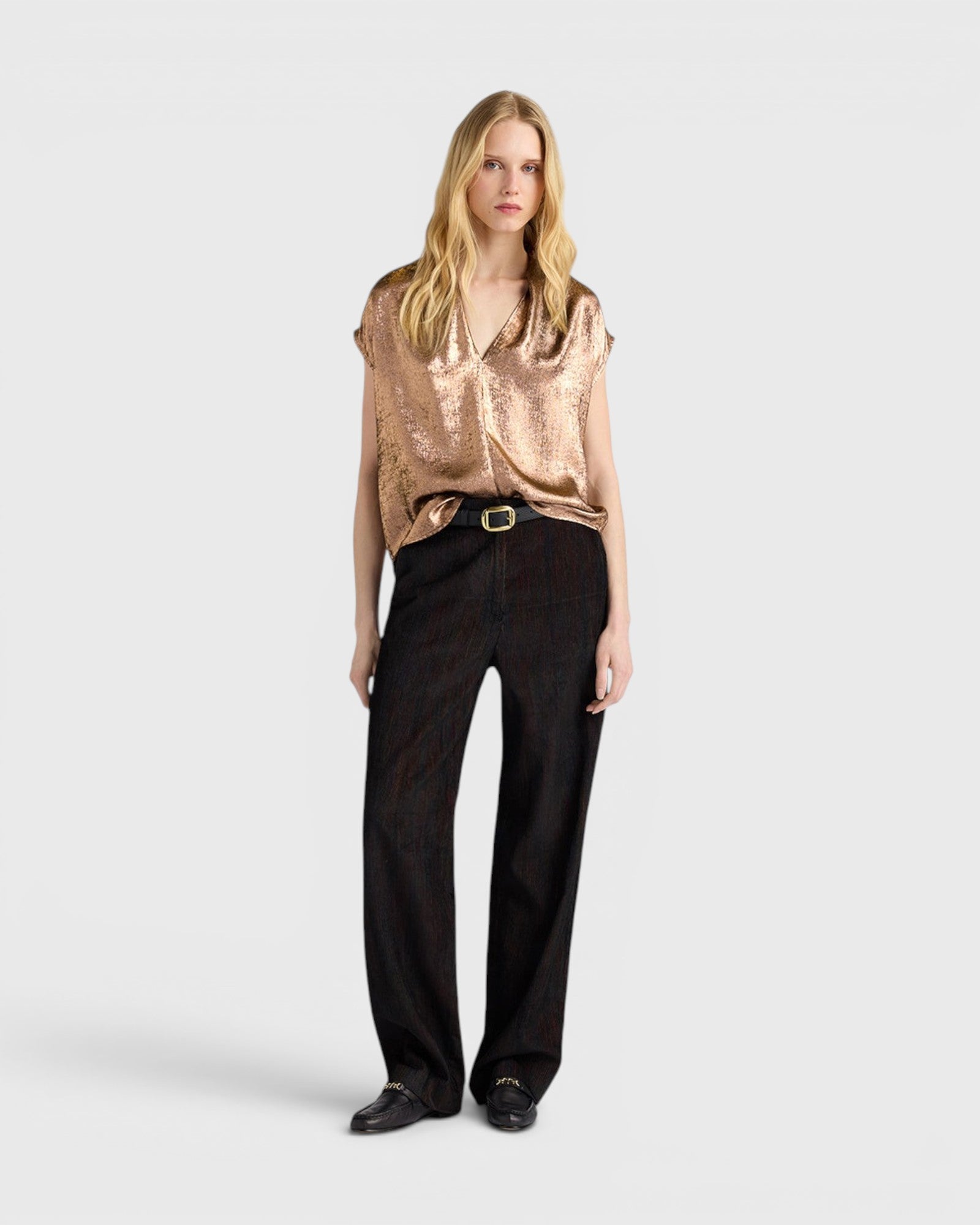 Model wearing a JONES + CO bronze sleeveless Hildra blouse with a V-neck, shawl collar, and fluid laminated fabric.