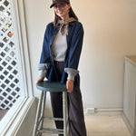 Woman wearing a brown JONES + CO baseball cap with white lettering, styled with a denim shirt and brown trousers.