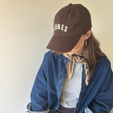 JONES + CO brown baseball cap with white embroidered lettering worn by a woman with a leopard print neck scarf