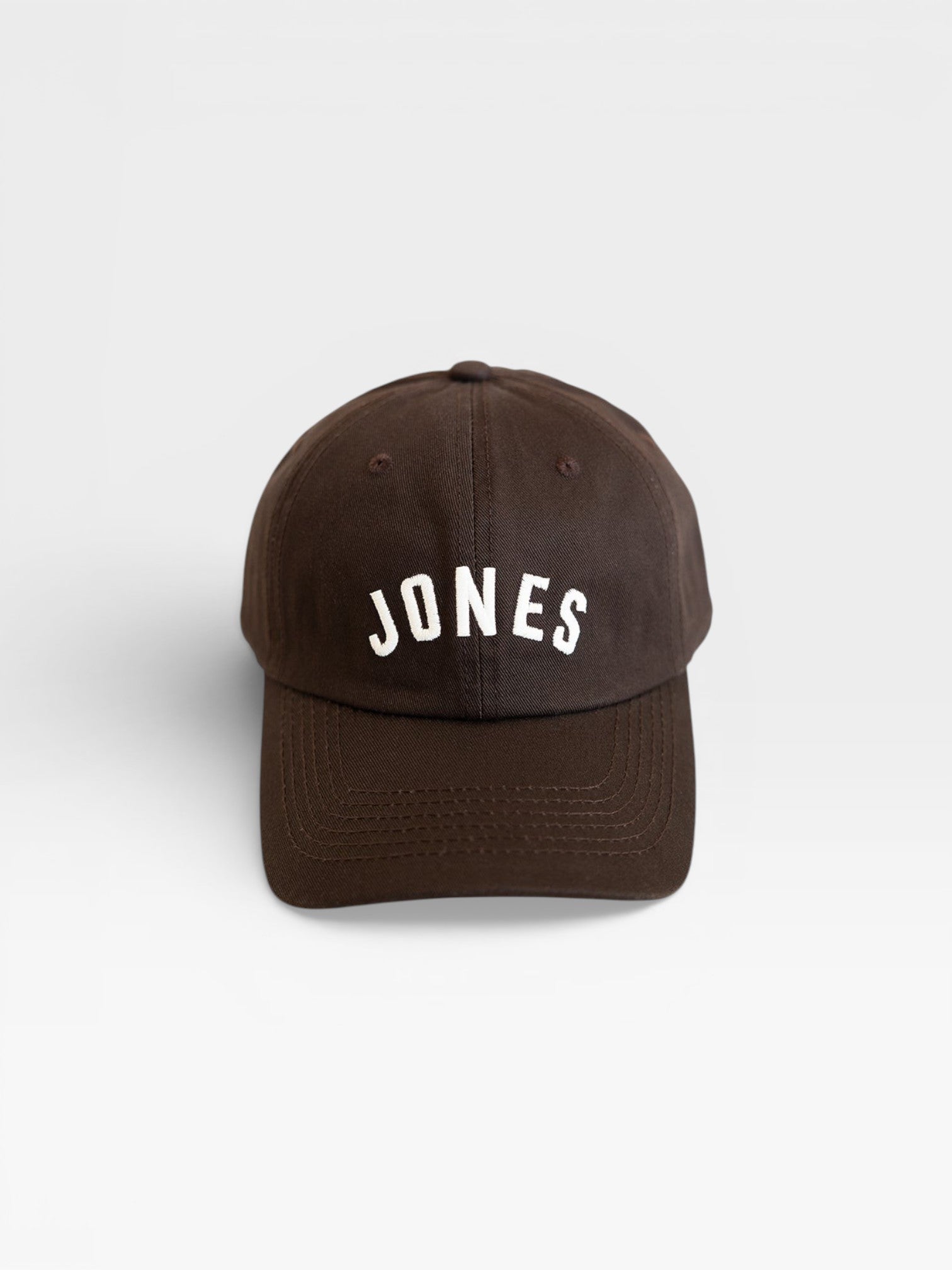 JONES + CO brown baseball cap with white embroidered JONES logo on the front, isolated on a white background.