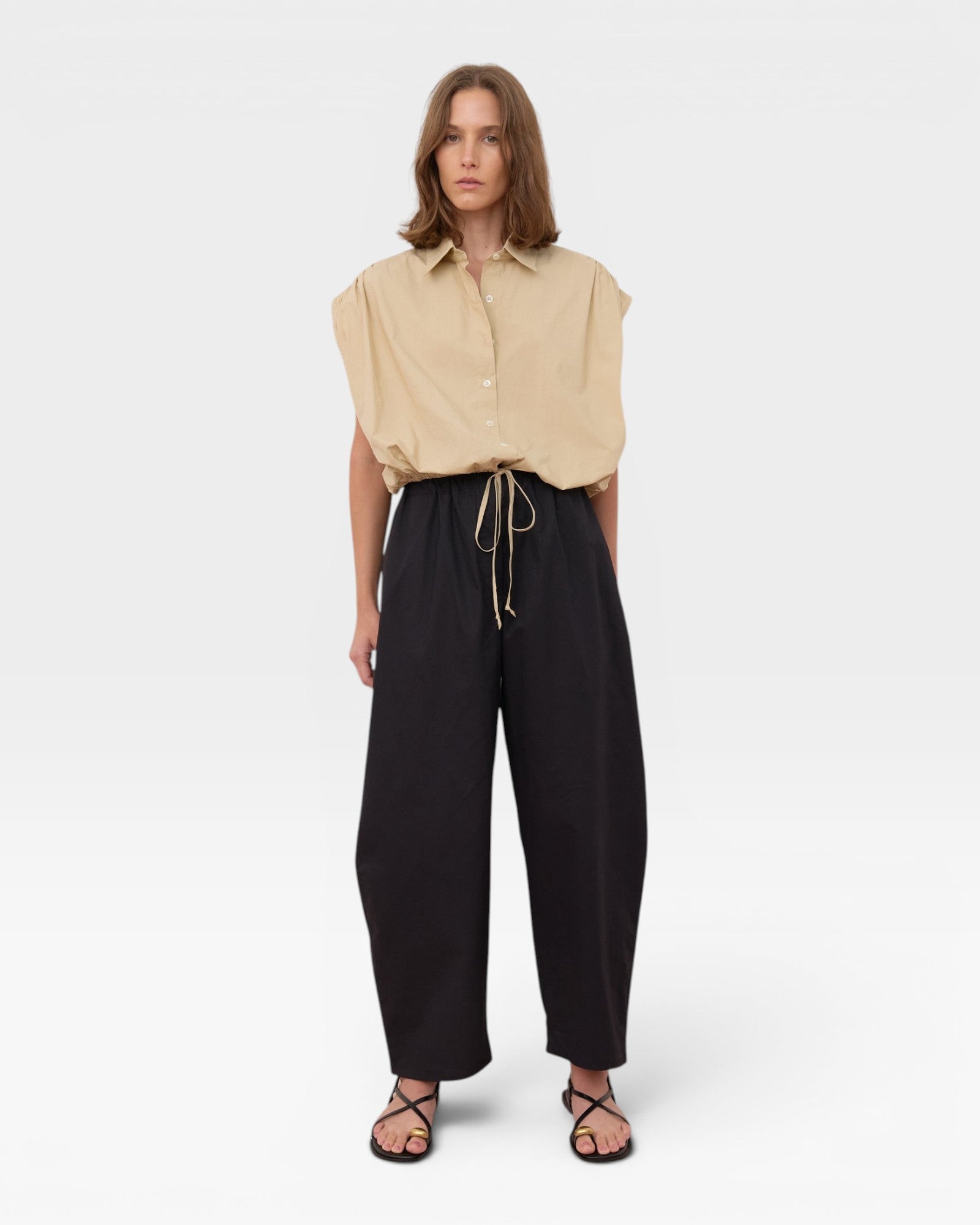 JONES + CO Cali Shirt in Sahara beige, a sleeveless collared button-up with cinched waist, paired with black wide-leg pants.
