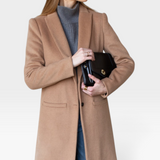 JONES + CO camel wool cashmere tailored coat with notch collar worn over a grey turtleneck and blue denim jeans.