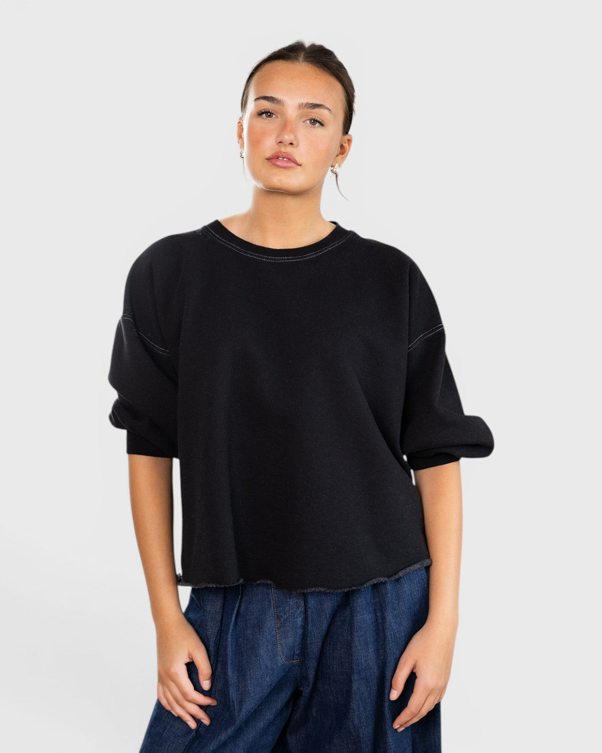 Model wearing a charcoal JONES + CO Fond crewneck sweatshirt with drop shoulders and a raw edge hemline.