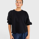 Model wearing a charcoal JONES + CO Fond crewneck sweatshirt with drop shoulders and a raw edge hemline.