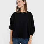 Model wearing a charcoal JONES + CO Fond sweatshirt with drop shoulders, cropped sleeves, and a raw edge hemline.