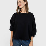 Model wearing a charcoal JONES + CO Fond sweatshirt with drop shoulders, cropped sleeves, and a raw edge hemline.
