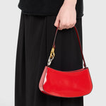 JONES + CO Ollie Bag in cherry-red polished leather with a crescent shape and metallic hardware held by a model.