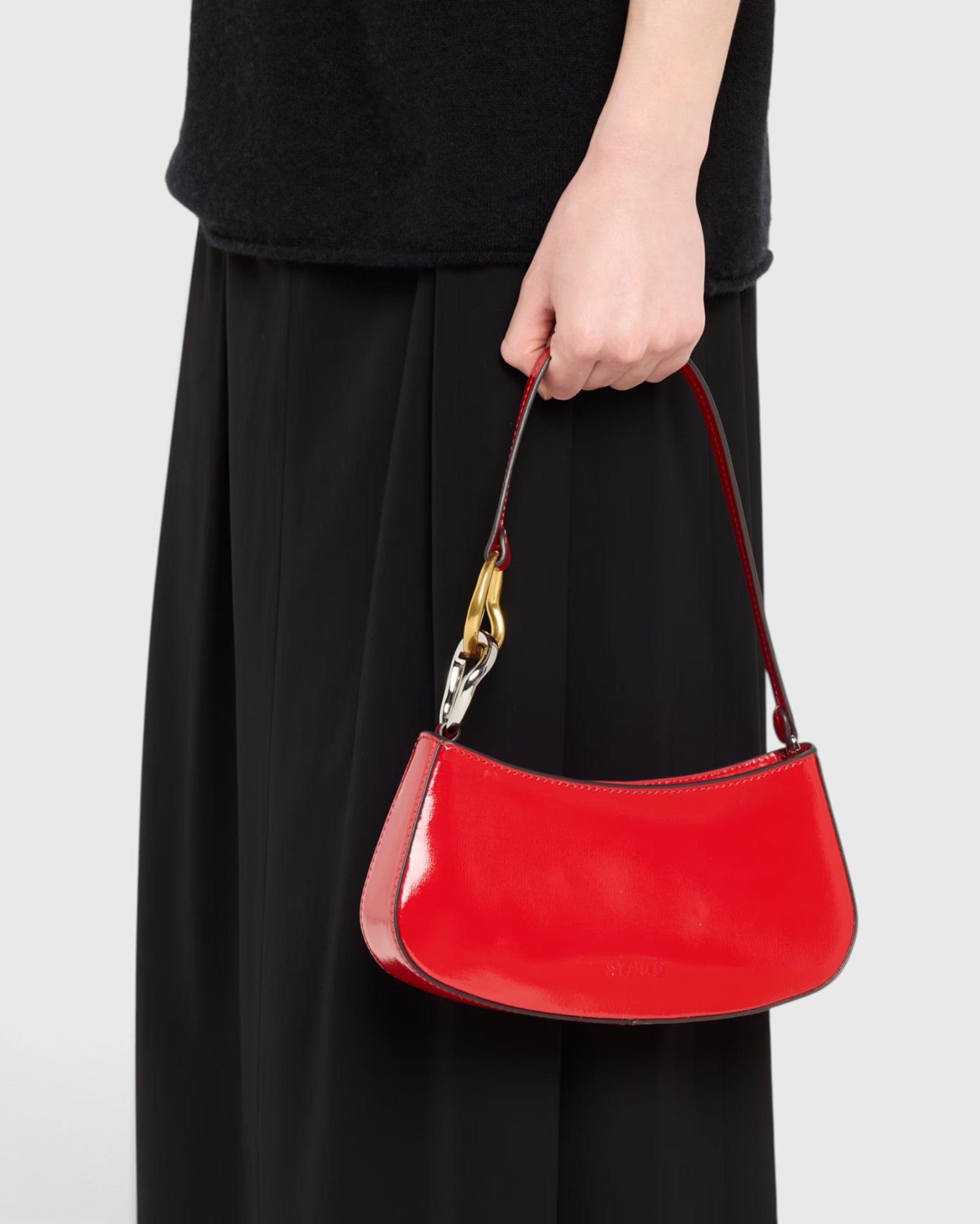 JONES + CO Ollie Bag in cherry-red polished leather with a crescent shape and metallic hardware held by a model.