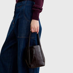JONES + CO chestnut lustre leather bucket bag with vertical paneling held by a person wearing dark denim jeans