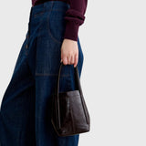 JONES + CO chestnut lustre leather bucket bag with vertical paneling held by a person wearing dark denim jeans