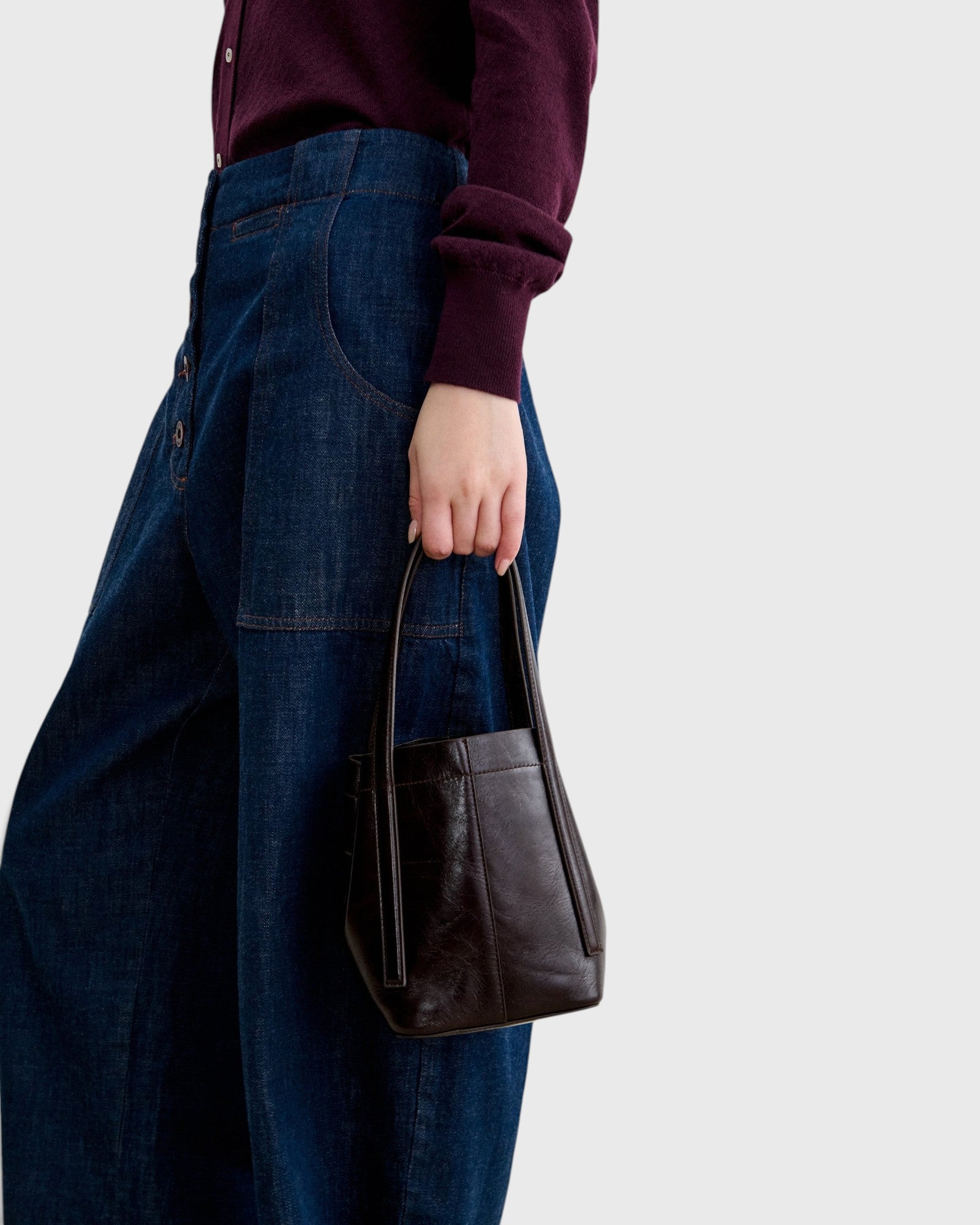 JONES + CO chestnut lustre leather bucket bag with vertical paneling held by a person wearing dark denim jeans