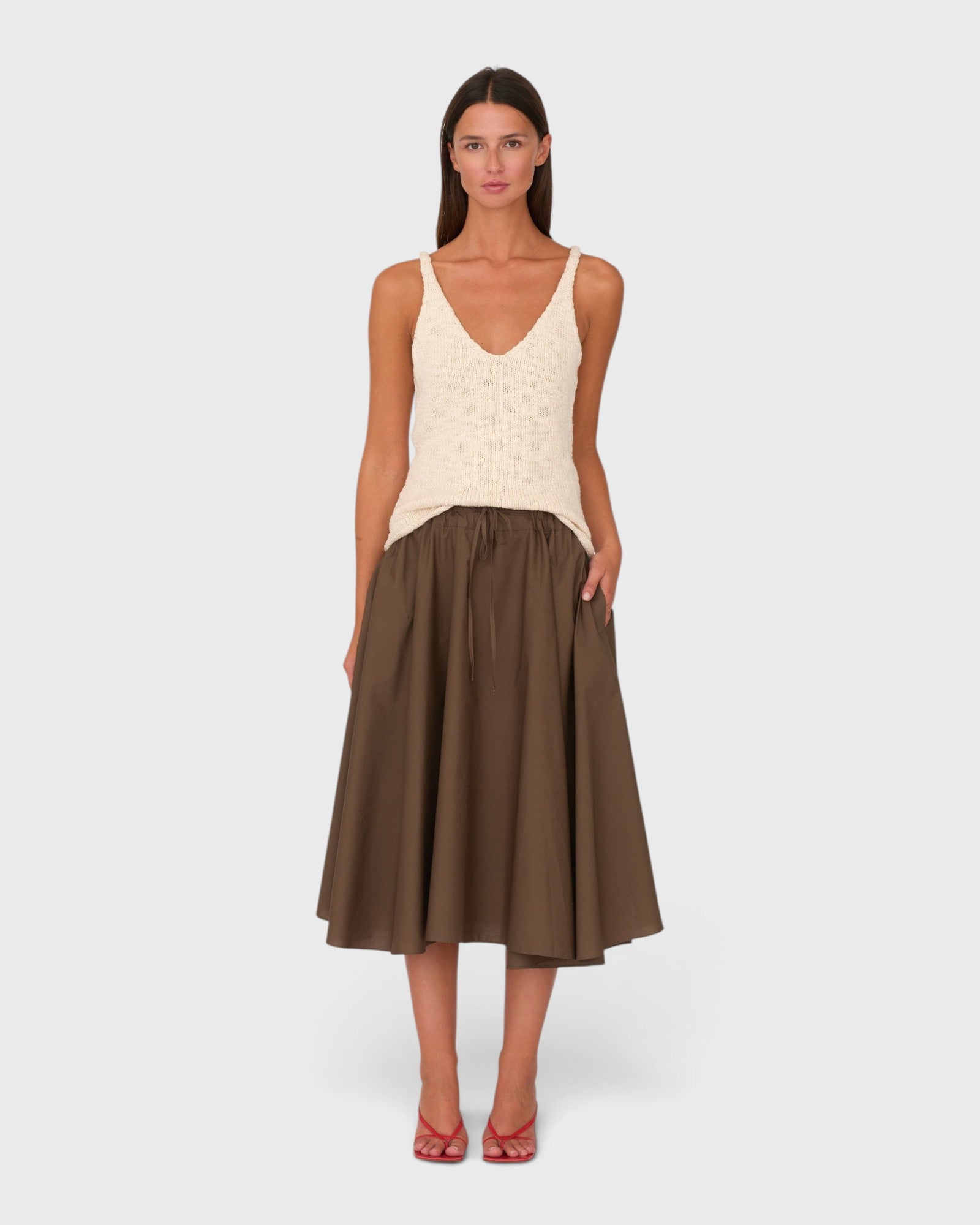 Model wearing a JONES + CO chocolate brown cotton poplin midi skirt with side pockets and a drawstring waistband.