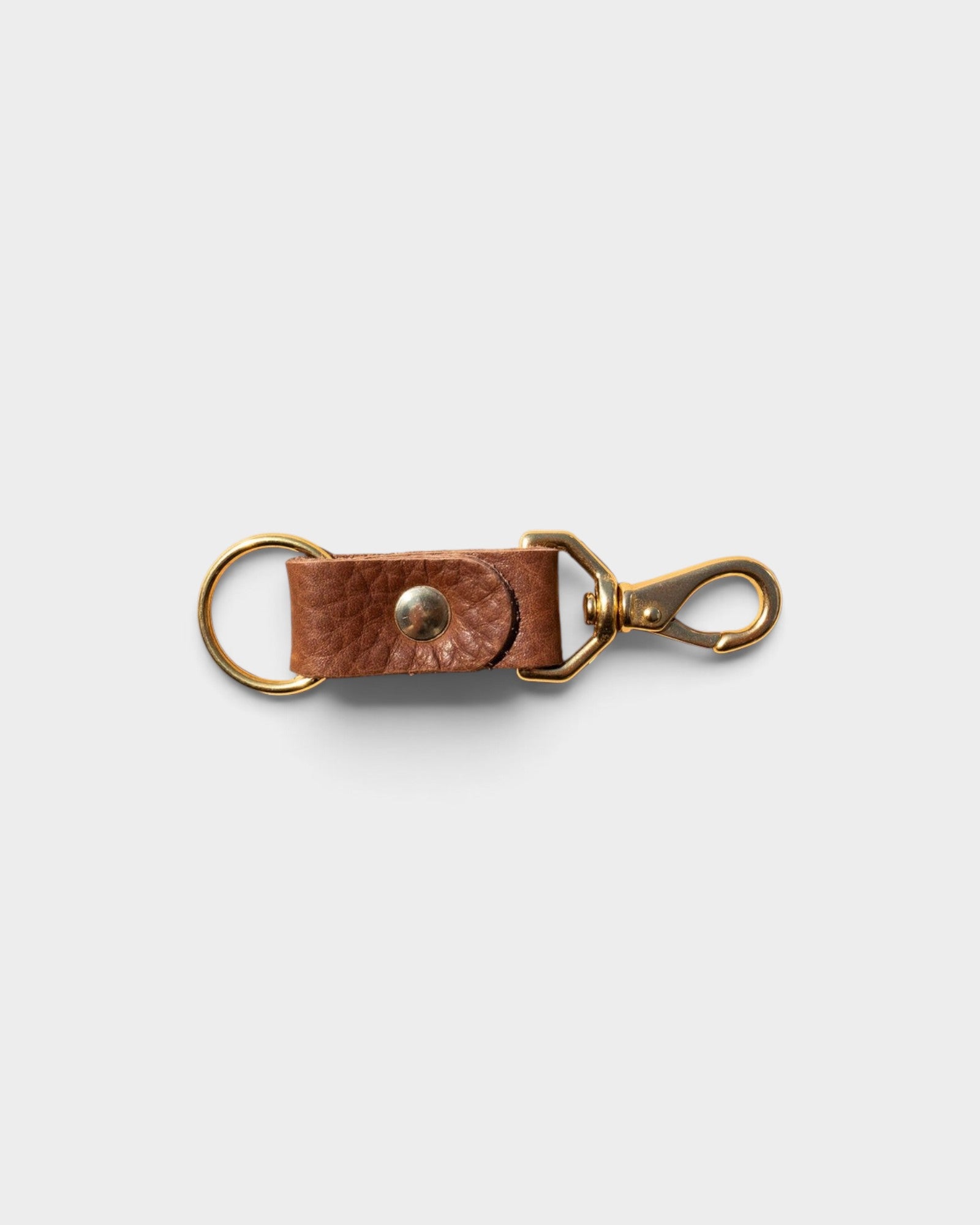 JONES + CO chocolate brown leather keychain with solid brass keyring and clip hardware on a light grey background.