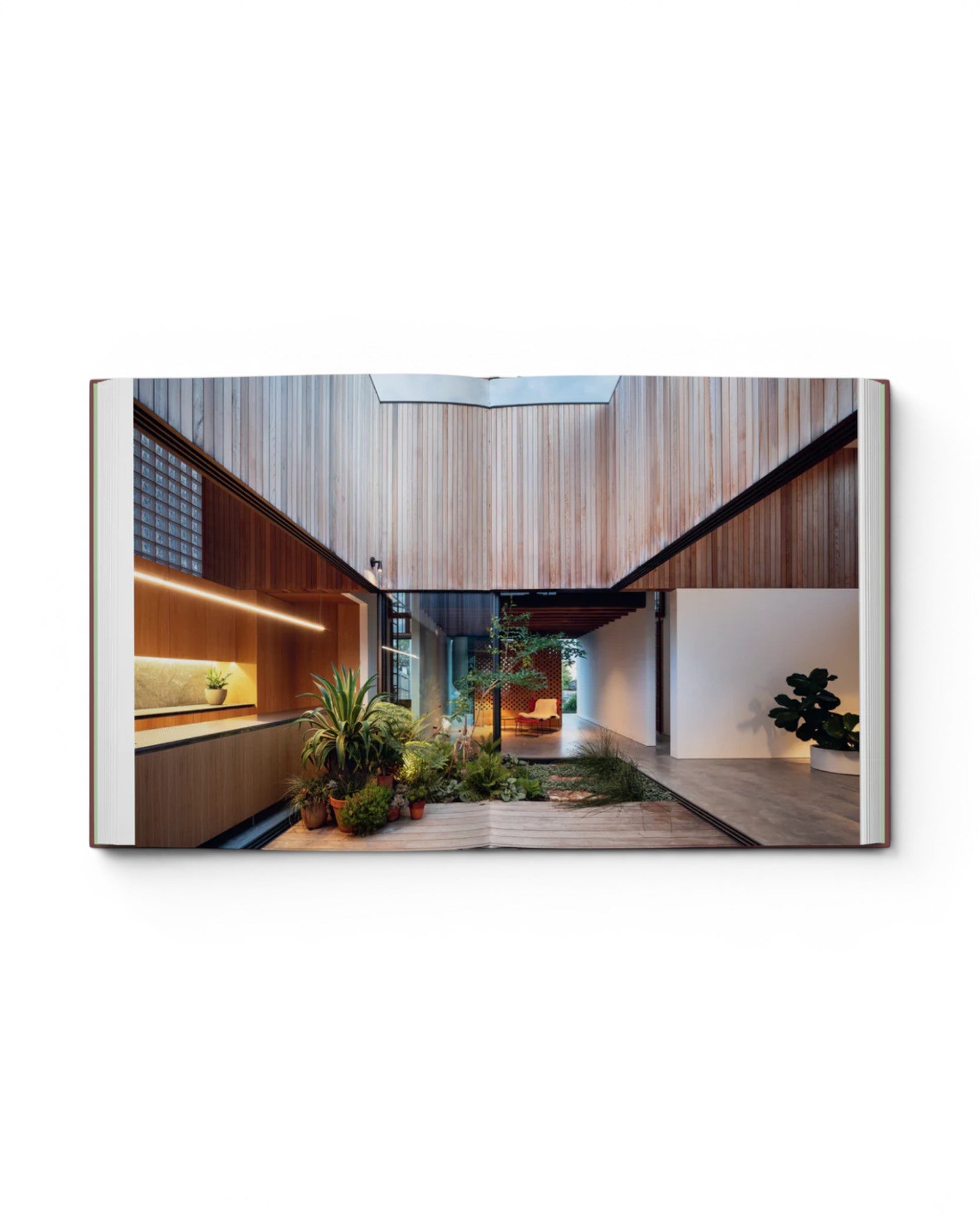 Open pages of JONES + CO Courtyard Homes book showing a modern residence with a central indoor garden and wood walls.