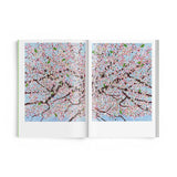 JONES + CO Damien Hirst Cherry Blossoms art book open to a spread featuring vibrant pink and blue floral paintings