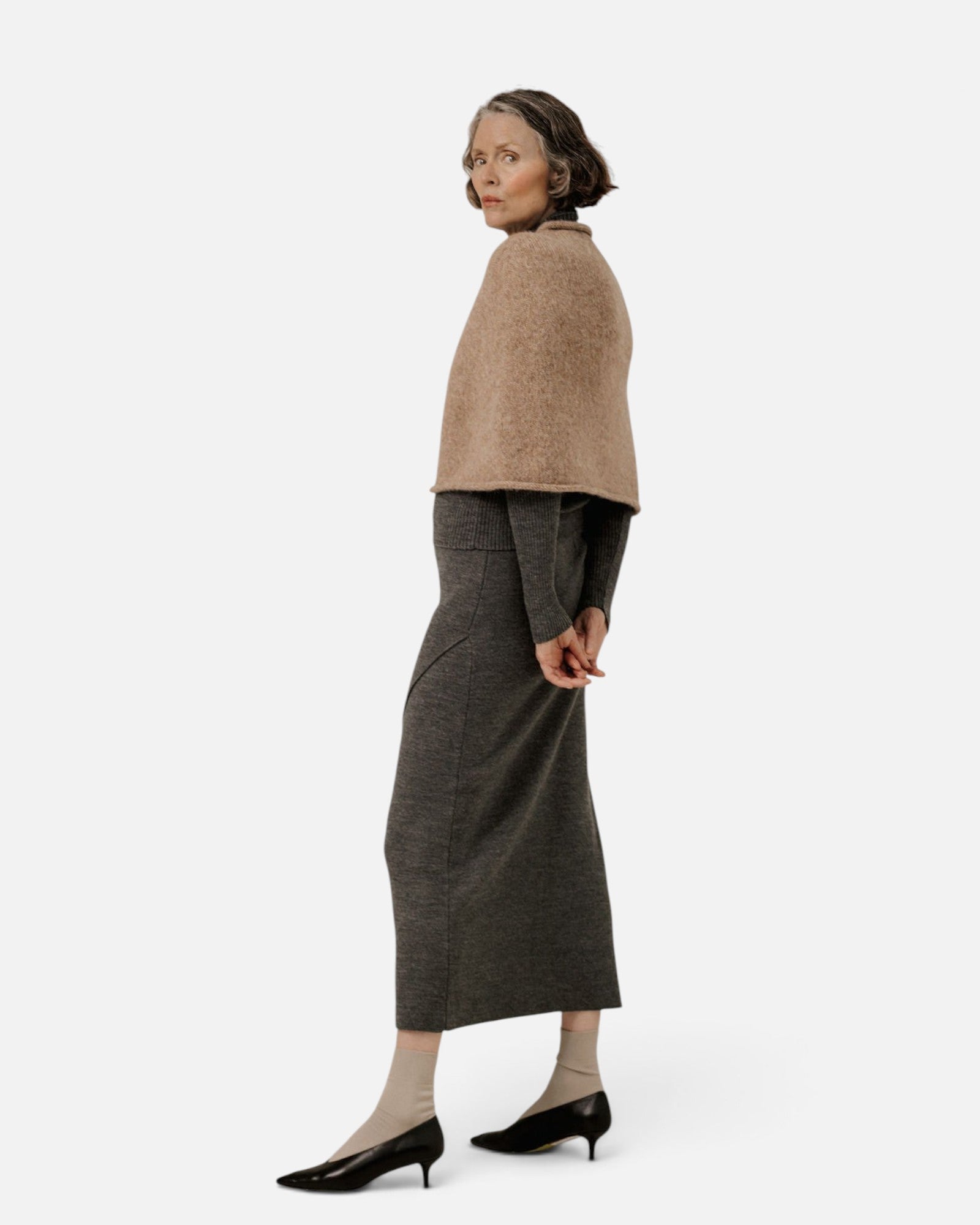 JONES + CO seamless dark fawn alpaca-blend poncho worn over a grey midi dress by a woman in a studio setting