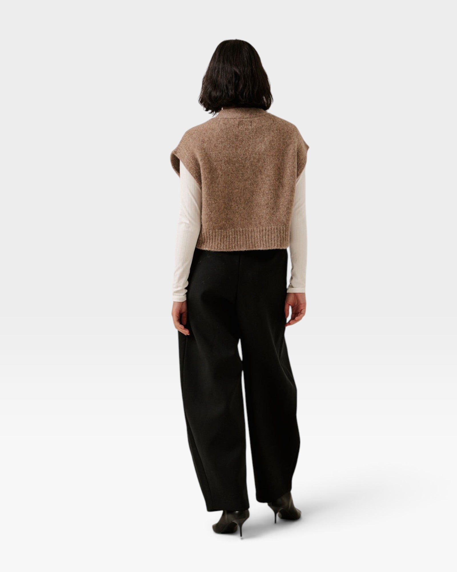 JONES + CO dark fawn alpaca blend button down vest worn over a white long sleeve top and black trousers, back view