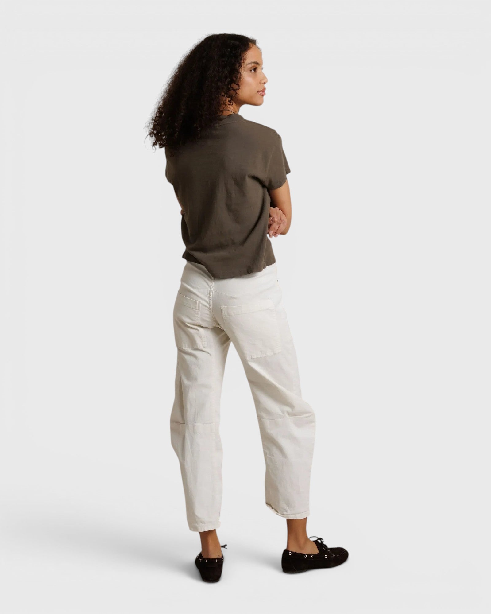 Model wearing JONES + CO dark olive recycled cotton V-neck tee with white trousers, back view
