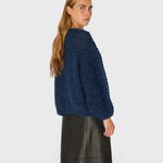 JONES + CO denim blue chunky alpaca bomber cardigan with pearl knit texture worn by a model, side view