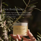 JONES + CO Dew Body Butter in a frosted jar with a white lid, held by a hand amidst greenery. Lavender Oak scent.