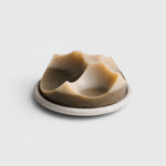 JONES + CO Erode Cardamom Vetiver soap with a unique sculpted shape on a matching round ceramic dish.