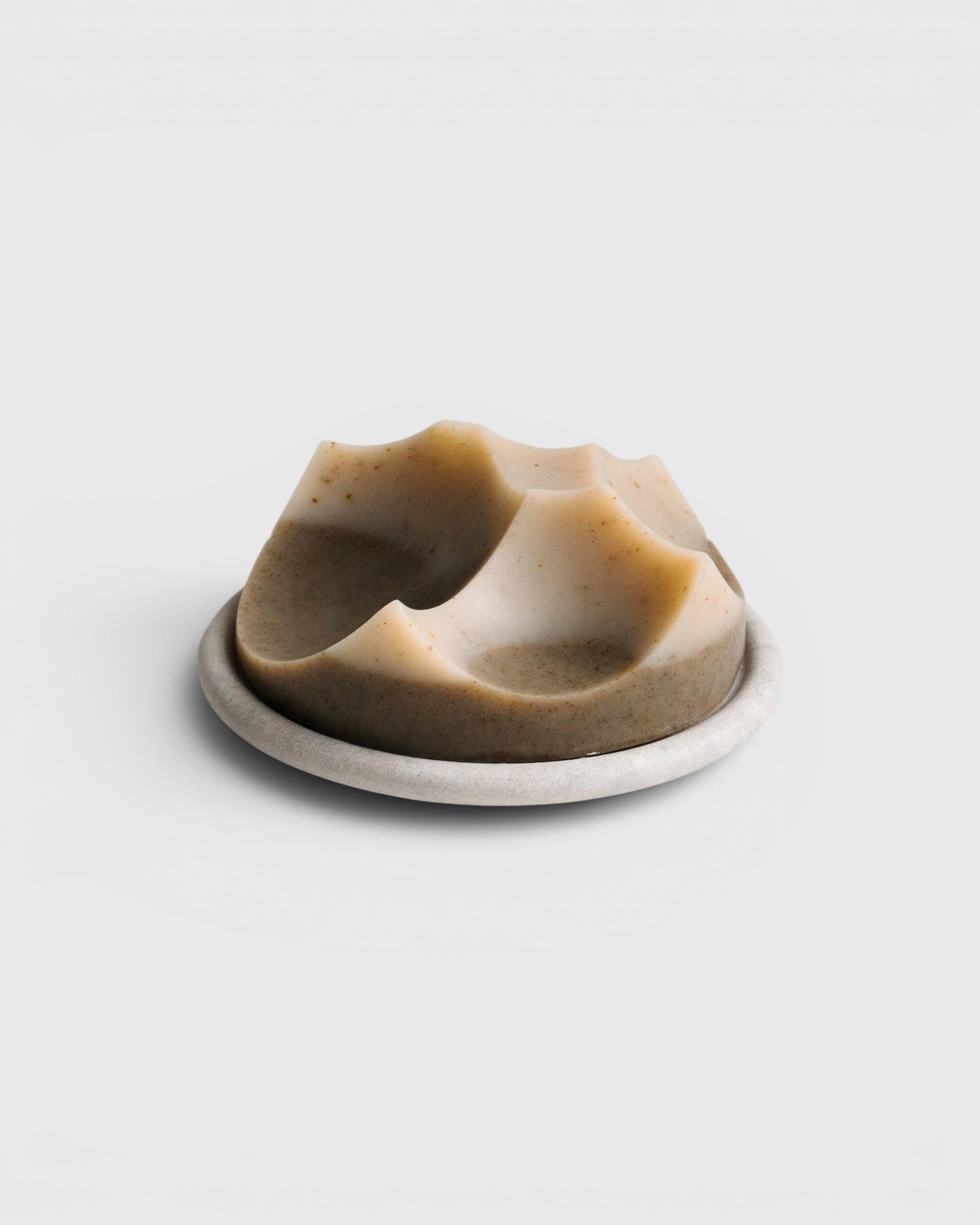 JONES + CO Erode Cardamom Vetiver soap with a unique sculpted shape on a matching round ceramic dish.