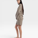 JONES + CO relaxed mid-length knit shorts in fog green with elastic waistband and drawstring. Model is wearing sandals.