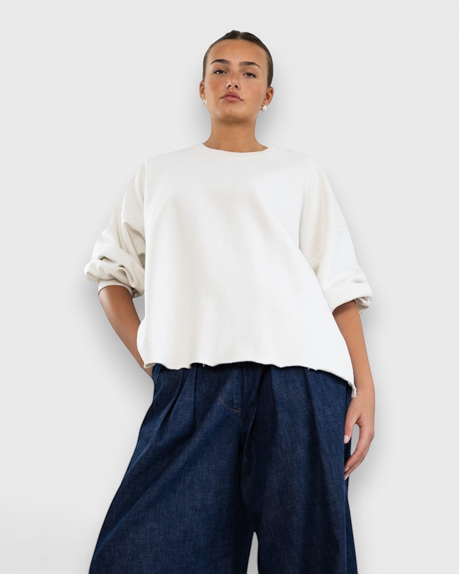Model wearing JONES + CO Fond crewneck sweatshirt in dirty white with drop shoulders and raw edge hemline.