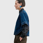 JONES + CO Fort Top in muddy indigo denim with a boxy silhouette, worn over a patterned shirt and brown trousers.