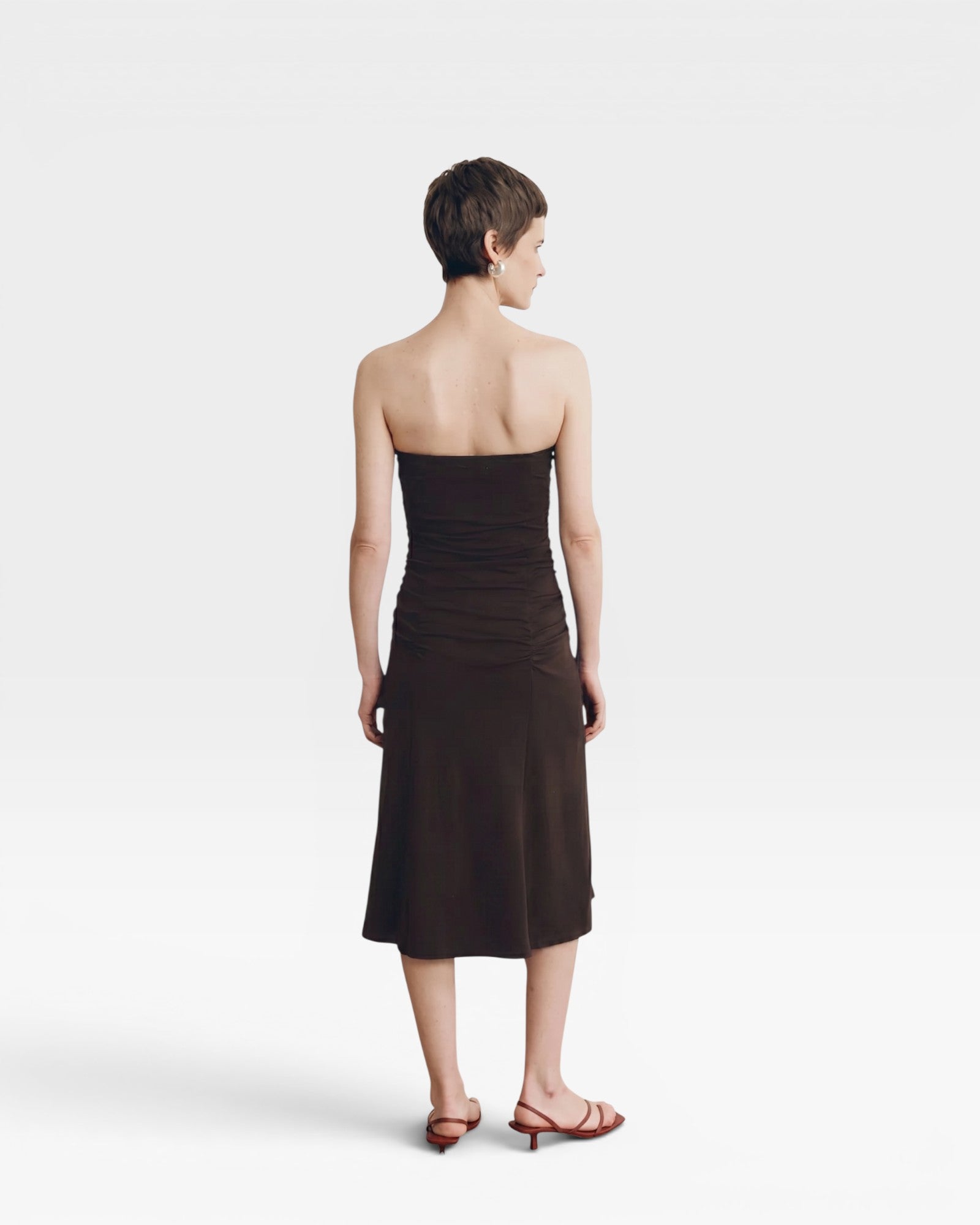 JONES + CO Gaia strapless midi dress in espresso. A model with short brown hair wears the dress from behind.