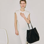 JONES + CO Scallop Tote in ganache suede held by a model wearing a white sleeveless dress against a neutral background.