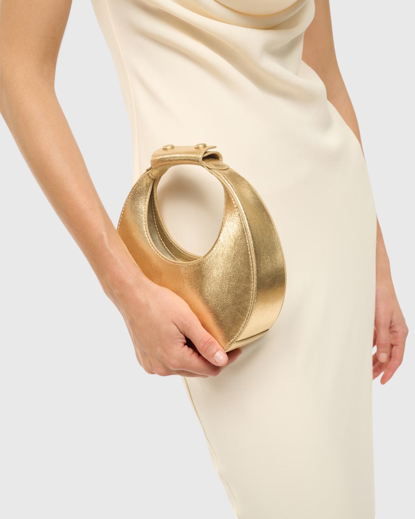 JONES + CO Good Night Moon evening bag in polished gold held in hand with a cream dress
