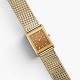JONES + CO Virgil Small watch with a gold rectangle case, ochre dial, and woven mesh bracelet on a white background.