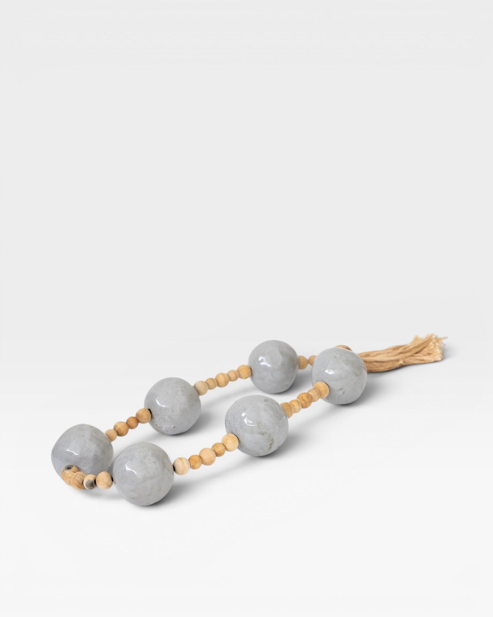 JONES + CO grey ceramic and wood beaded hanging wall art with tassel detail.