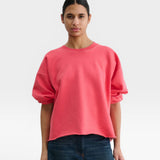 Model wearing a JONES + CO guava pink crewneck sweatshirt with drop shoulders, cropped sleeves, and raw edge hem.