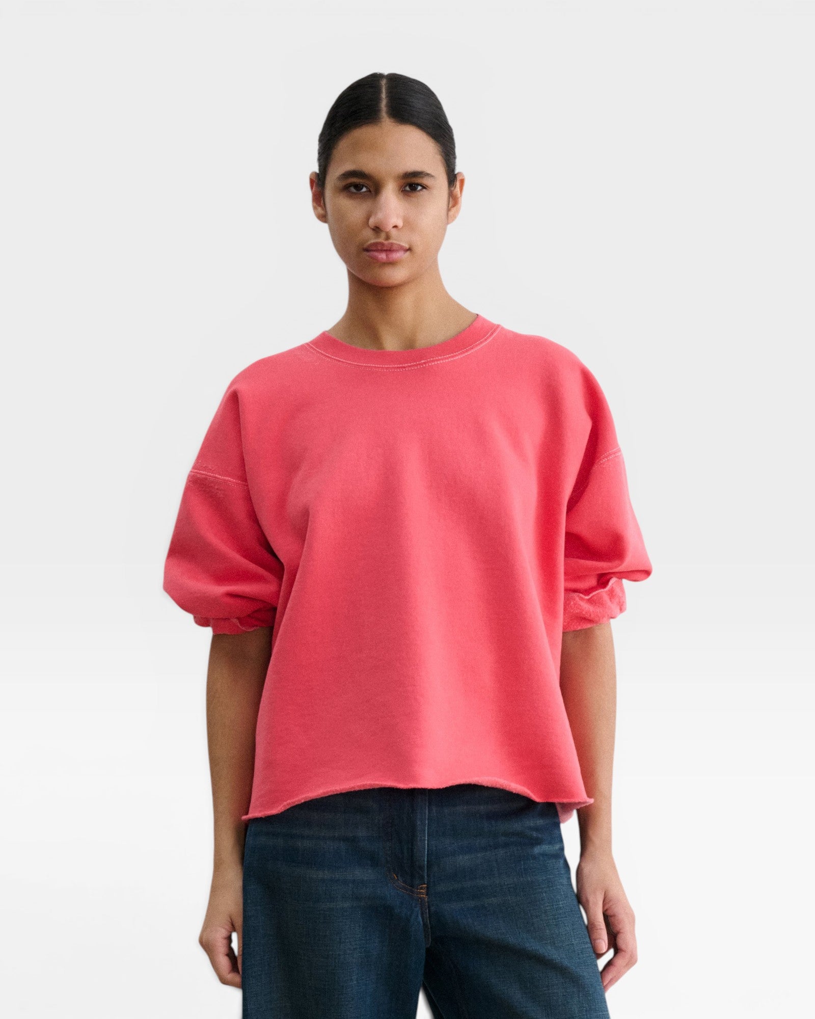 Model wearing a JONES + CO guava pink crewneck sweatshirt with drop shoulders, cropped sleeves, and raw edge hem.