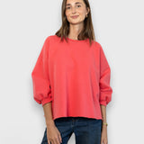 Model wearing a JONES + CO guava pink Fond crewneck sweatshirt with drop shoulders and raw edge hemline.