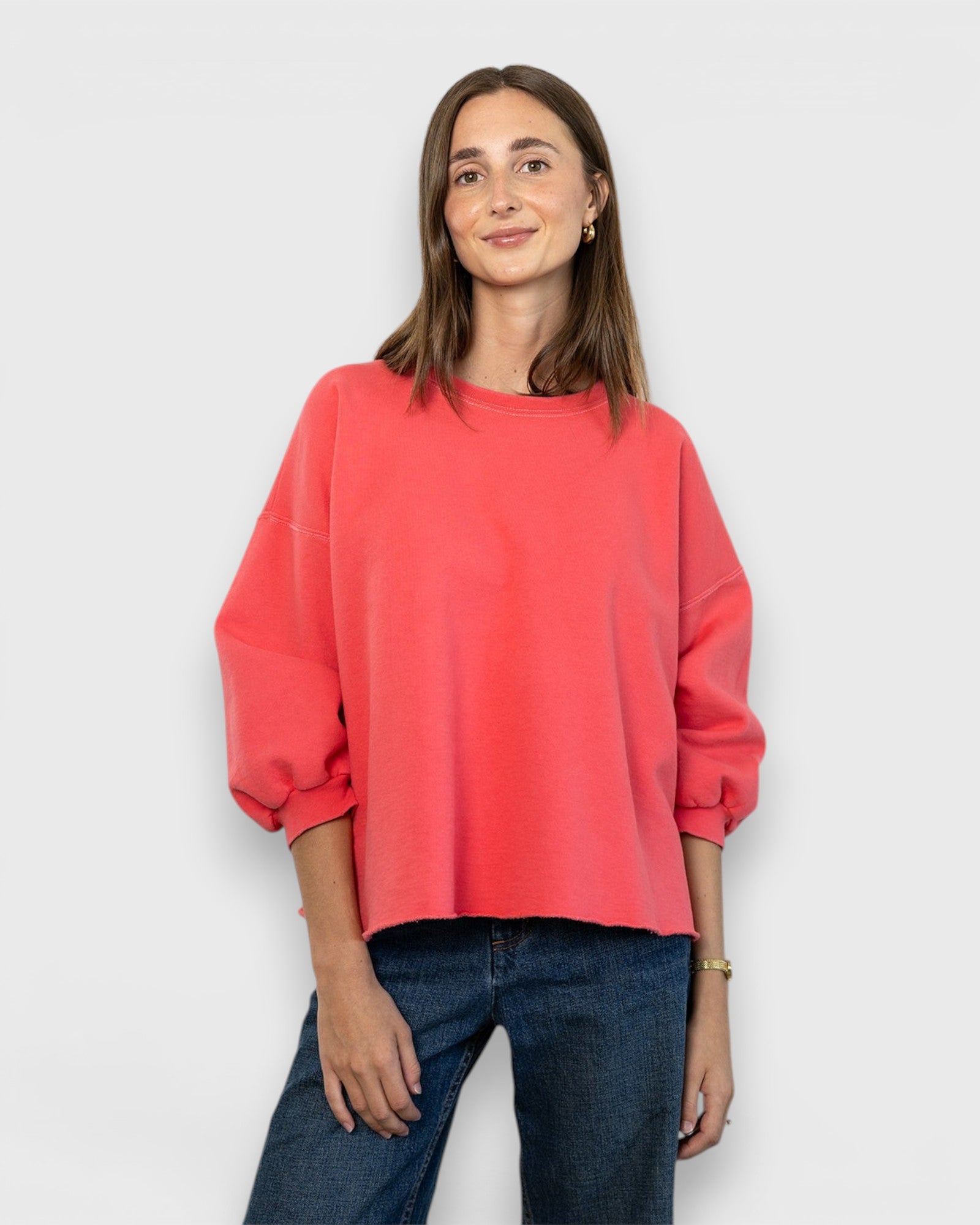 Model wearing a JONES + CO guava pink Fond crewneck sweatshirt with drop shoulders and raw edge hemline.