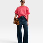 Model wearing a JONES + CO guava pink crewneck sweatshirt with drop shoulders and raw hem, paired with wide-leg jeans.