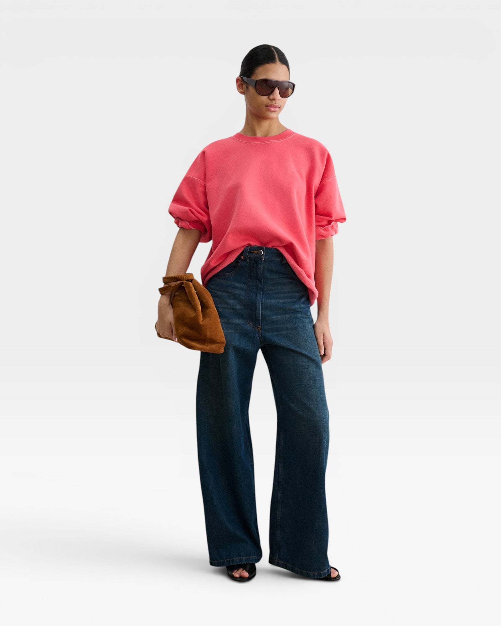 Model wearing a JONES + CO guava pink crewneck sweatshirt with drop shoulders and raw hem, paired with wide-leg jeans.